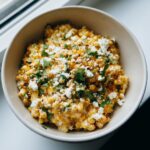 A close-up overhead view of a bowl of street corn dip, topped with crumbled feta cheese and fresh cilantro.
