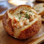 Close-up of a crusty bread bowl generously filled with creamy stuffed seafood, garnished with parsley.