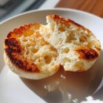 Close-up of a homemade english muffin split open, showing its signature nooks and crannies texture, toasted golden brown.