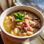 A close-up of a bowl of hearty white bean and ham soup, garnished with fresh parsley.