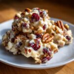 A close-up of white chocolate cranberry pecan clusters on a white plate, showing the creamy white chocolate, tart cranberries, and crunchy pecans.