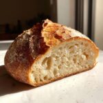 A rustic loaf of homemade bread, cut in half to show the airy crumb structure and golden crust.