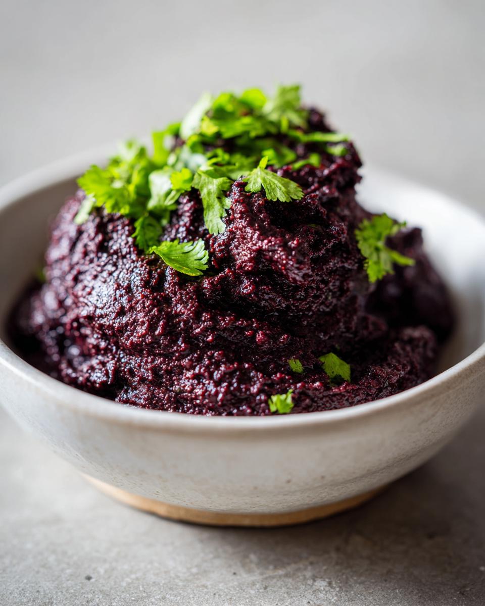 Close-up of a deep purple-black bean dip, textured and mounded in a light bowl, topped with fresh cilantro.