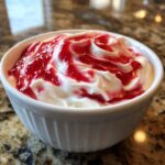 A white ramekin filled with creamy strawberry cheesecake dip swirled with bright red strawberry topping.