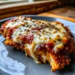 Close-up of a crispy air fryer chicken parmesan topped with melted mozzarella, marinara sauce, and dried herbs.