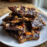 A stack of broken pieces of homemade almond chocolate toffee recipe on a white plate.