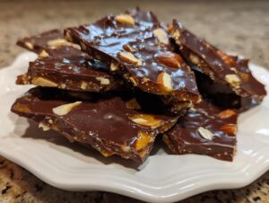 Close-up of broken pieces of homemade almond chocolate toffee recipe stacked on a white plate.