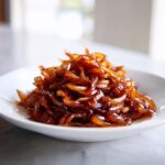 A mound of rich, dark brown caramelized onions served on a small white plate.