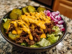 A close-up of a delicious cheeseburger bowl featuring ground beef, melted cheese sauce, pickles, and diced red onion over lettuce.