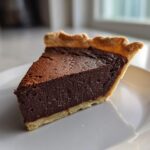 A close-up slice of rich, dark chocolate fudge pie with a flaky crust on a white plate.