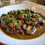 Close-up of steak smothered in rich, brown mushroom sauce and topped with fresh chopped parsley.
