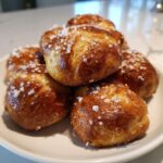 A close-up stack of freshly baked, golden brown pretzel bites topped with coarse sea salt.