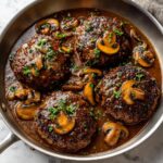 Four perfectly cooked salisbury steak patties simmering in rich brown mushroom gravy, garnished with fresh parsley.