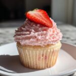 A single, delicious strawberry cupcake with pink frosting and a fresh strawberry slice on top.