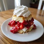 A delicious homemade strawberry shortcake layered with macerated strawberries and topped with a swirl of whipped cream.