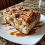 A close-up of a moist slice of apple bread pudding drizzled with caramel and vanilla glaze.