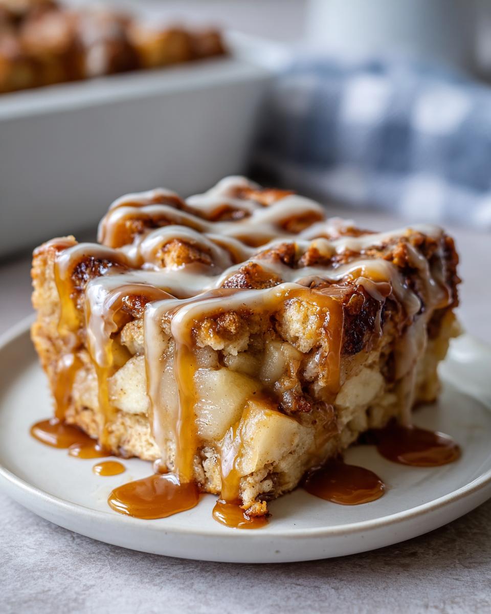 Close-up of a square slice of apple bread pudding topped with vanilla glaze and dripping caramel sauce.