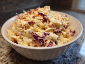 A white bowl filled with creamy apple cranberry coleslaw featuring shredded cabbage, carrots, and dried cranberries.