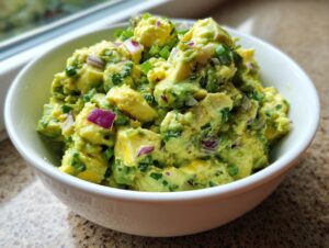 Close-up of chunky avocado egg salad mixed with diced red onion and green onions in a white bowl.