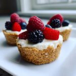 Close-up of a fresh mini cheesecake bite topped with a raspberry, blackberry, strawberry, and blueberry.