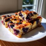 Close-up of three golden-brown squares of blueberry sheet pan pancakes stacked on a white plate.