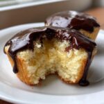 Close-up of a boston cream pie cupcakes cut in half showing vanilla cake, pastry cream filling, and dripping chocolate ganache.
