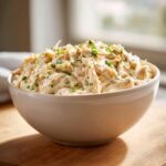 A white bowl filled with creamy, shredded cream cheese chicken chili, garnished with green chives.