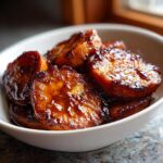 Close-up of thick-cut candied sweet potatoes glistening with a dark, rich glaze in a white bowl.