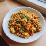 A white bowl filled with colorful cauliflower fried rice, mixed with scrambled egg, carrots, peas, and topped with green onions.
