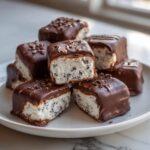 A stack of chocolate-covered cool whip candy squares with visible cookie pieces inside, resting on a white plate.