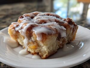 A single, gooey cinnamon roll apple pie swirl topped with thick white icing, sitting on a white plate.