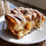 Close-up of a soft, glazed cinnamon roll apple pie slice showing tender dough and apple filling.
