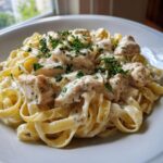 Close-up of fettuccine pasta coated in rich white sauce with chunks of seasoned chicken, garnished with fresh parsley, a perfect chicken alfredo.