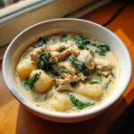 Close-up of a hearty bowl of creamy chicken and gnocchi soup with wilted spinach.