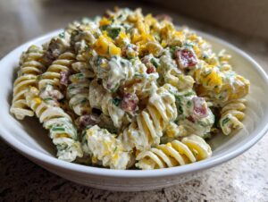 Close-up of creamy pickle pasta salad made with rotini pasta, visible chunks of pickles, and herbs in a white bowl.
