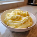 A white bowl filled with creamy roasted garlic mashed potatoes topped with melted butter.