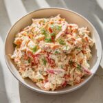 A bowl filled with creamy seafood salad mixed with red peppers and topped with fresh dill.