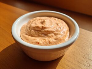A small white bowl filled with creamy, orange-tinted smash burger sauce speckled with red spices.