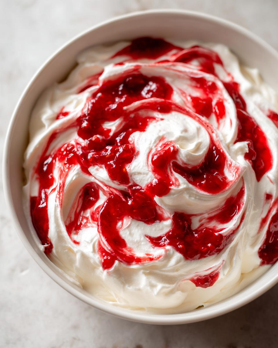 Close-up of creamy white strawberry cheesecake dip swirled dramatically with bright red strawberry topping.