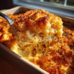 A spoonful of creamy tuna pasta lifted from a baking dish, showing a golden, crispy breadcrumb topping.