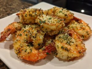 Close-up of several crispy, breaded air fryer shrimp seasoned with parsley, piled on a white serving plate.