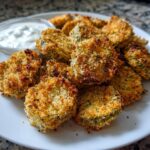 A plate piled high with golden brown, crispy Fried Pickles served alongside a small bowl of white dipping sauce.