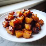A pile of perfectly roasted and glazed sweet potatoes cubes on a white plate.