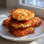 A stack of three perfectly golden and crispy potato latkes on a white plate, showing shredded texture.
