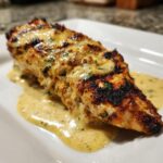 Close-up of a perfectly grilled fiesta lime chicken breast covered in a creamy, cheesy sauce with visible herbs.