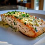 Close-up of a perfectly cooked fillet from a baked salmon recipe, topped with garlic butter and fresh parsley.