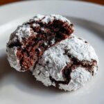 Close-up of two fudgy chocolate crinkle cookies dusted heavily with powdered sugar, one broken open.