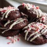 A stack of fudgy double chocolate peppermint cookies drizzled with white icing and topped with crushed candy canes.