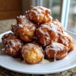 A tempting stack of golden brown apple fritter bites drizzled with sweet white glaze and powdered sugar.
