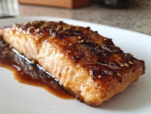 Close-up of a perfectly cooked salmon fillet topped with a thick, dark glaze and sesame seeds.
